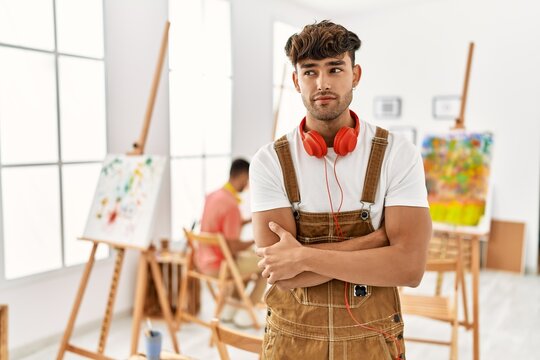 Young hispanic man at art studio smiling looking to the side and staring away thinking.