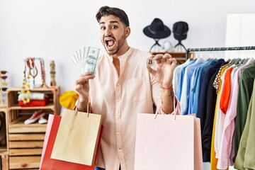 Young hispanic man holding shopping bags, dollars and bitcoin celebrating crazy and amazed for success with open eyes screaming excited.