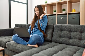 Obraz premium Young chinese girl wearing casual clothes working using laptop at home celebrating victory with happy smile and winner expression with raised hands