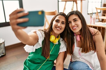 Two latin paint students smiling happy make selfie by the smartphone at art school.
