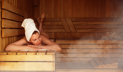 Young woman relaxing and sweating in hot sauna wrapped in towel. Girl In Sauna. Interior of Finnish...