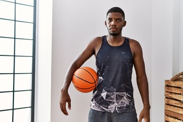 Young african american man holding basketball ball at home thinking attitude and sober expression...