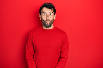 Handsome man with beard wearing casual red sweater making fish face with lips, crazy and comical gesture. funny expression.