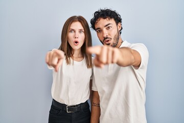 Young couple wearing casual clothes standing together pointing with finger surprised ahead, open mouth amazed expression, something on the front