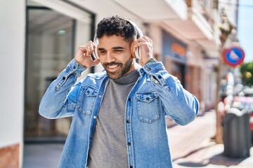 Young hispanic man smiling confident listening to music at street
