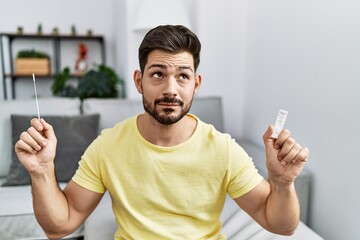Young man with beard holding coronavirus infection nasal test smiling looking to the side and...