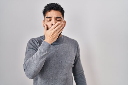 Hispanic man with beard standing over white background bored yawning tired covering mouth with hand. restless and sleepiness.