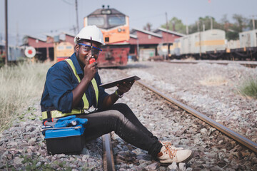 Fototapeta na wymiar African man technician engineer check and repair the train on railway with holding tablet and talking by radio communication or walkie talkie
