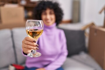 Young middle east woman smiling confident drinking glass of wine at new home