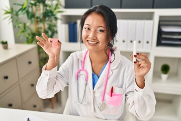 Young asian doctor woman holding menstrual cup and tampon smiling with a happy and cool smile on face. showing teeth.