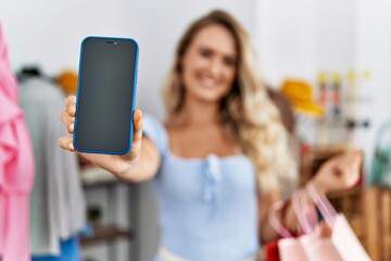 Young woman customer showing smartphone app holding shopping bags at clothing store