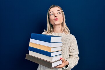 Beautiful caucasian woman holding a pile of books looking at the camera blowing a kiss being lovely and sexy. love expression.