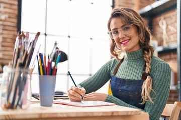 Young woman artist drawing on notebook sitting on table at art studio