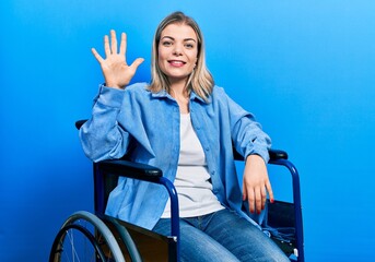 Beautiful caucasian woman sitting on wheelchair showing and pointing up with fingers number five while smiling confident and happy.