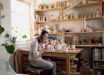 a woman in a carpentry workshop is engaged in coloring handmade wooden toys.