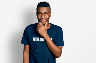 Fototapeta premium Young african american man wearing volunteer t shirt looking confident at the camera smiling with crossed arms and hand raised on chin. thinking positive.