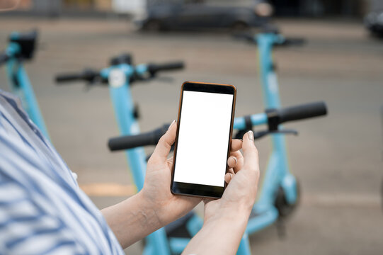 Woman Holds In Her Hands A Smartphone To Pull Down The Screen. Pays For Renting An Electric Scooter