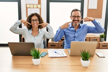 Middle age hispanic woman and man sitting with laptop at the office smiling cheerful showing and pointing with fingers teeth and mouth. dental health concept.