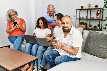 Group of middle age friends using laptop and smartphone sitting on the sofa at home.