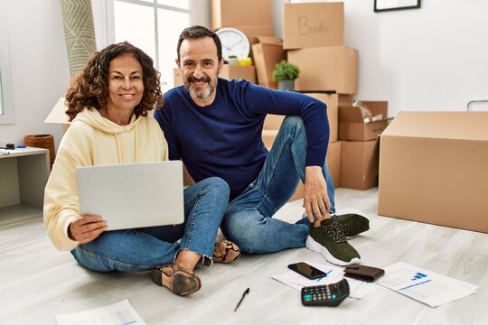 Middle Age Hispanic Couple Smiling Happy Controlling Family Economy. Sitting On The Floor At New Home.