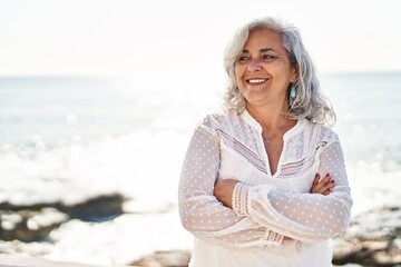 Middle age woman smiling confident standing with arms crossed gesture at seaside
