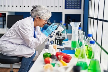 Middle age woman wearing scientist uniform using microscope at laboratory