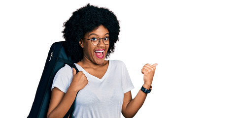 Young african american woman wearing guitar case pointing thumb up to the side smiling happy with open mouth