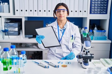 Fototapeta premium Hispanic young woman working at scientist laboratory relaxed with serious expression on face. simple and natural looking at the camera.