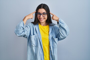Young hispanic woman standing over blue background smiling pointing to head with both hands finger, great idea or thought, good memory