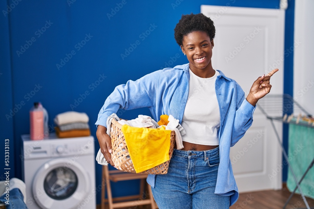 Sticker african american woman holding laundry basket smiling happy pointing with hand and finger to the sid