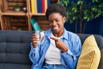 African american woman drinking glass of water smiling happy pointing with hand and finger