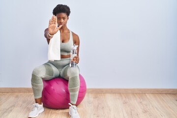 African american woman wearing sportswear sitting on pilates ball doing stop sing with palm of the...