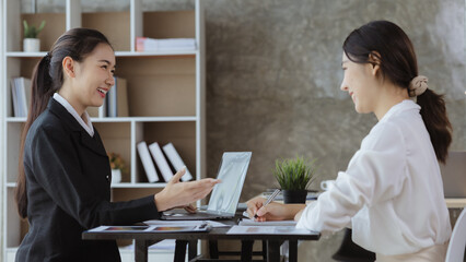 Atmosphere in the office of a startup company, two female employees are discussing, brainstorming ideas to working on summaries and marketing plans to increase sales and prepare reports to managers.