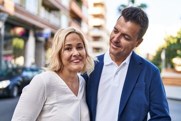 Middle age man and woman couple hugging each other standing at street