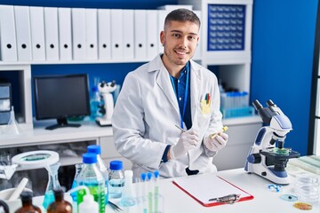 Young hispanic man scientist writing on test tube at laboratory