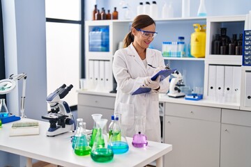 Fototapeta premium Middle age woman wearing scientist uniform writing on clipboard at laboratory