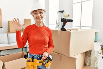 Middle age grey-haired woman wearing hardhat standing at new home showing and pointing up with fingers number five while smiling confident and happy.