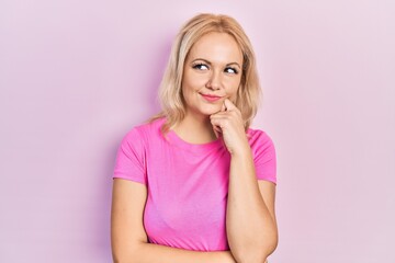 Young blonde woman wearing casual pink t shirt thinking concentrated about doubt with finger on chin and looking up wondering