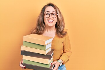 Middle age caucasian woman holding a pile of books smiling and laughing hard out loud because funny crazy joke.