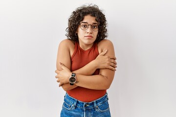 Young hispanic woman wearing glasses standing over isolated background shaking and freezing for winter cold with sad and shock expression on face