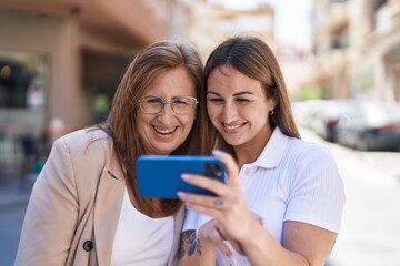 Mother and daughter using smartphone standing together at street