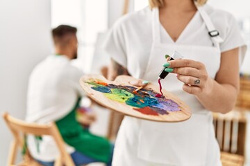 Young caucasian couple drawing at art studio. Girl mixing colors on palette.