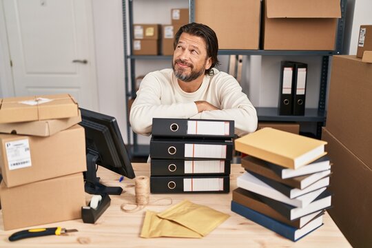Handsome middle age man working at small business ecommerce smiling looking to the side and staring away thinking.