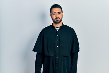 Handsome hispanic man with beard wearing catholic priest robe looking sleepy and tired, exhausted for fatigue and hangover, lazy eyes in the morning.