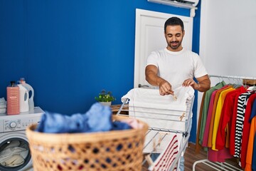 Young hispanic man smiling confident hanging clothes on clothesline at laundry room