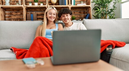 Young couple watching film and eating popcorn sitting on the sofa at home.