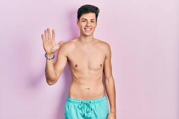 Young hispanic man wearing swimwear shirtless showing and pointing up with fingers number five...