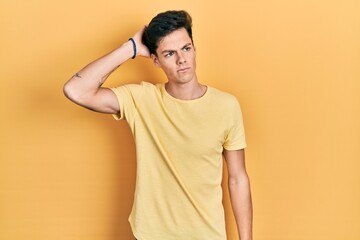 Young hispanic man wearing casual yellow t shirt confuse and wondering about question. uncertain with doubt, thinking with hand on head. pensive concept.