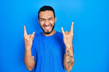 Hispanic man with beard wearing casual blue t shirt shouting with crazy expression doing rock symbol with hands up. music star. heavy concept.