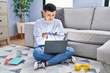 Non binary person studying using computer laptop sitting on the floor skeptic and nervous, disapproving expression on face with crossed arms. negative person.
